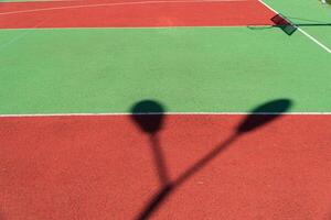 Striking shadows cast by nearby poles mingle with the bright colors of a freshly maintained tennis court on a sunny day photo