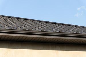 Textured roofing material on a modern home reflects sunlight under a clear blue sky, showcasing craftsmanship and design elements photo