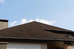 The roof of a contemporary house is highlighted against a bright blue sky with a few soft clouds visible above photo