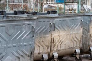 Several large metal waste containers are lined up in a park area, indicating a focus on waste management in an urban environment photo