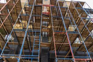 Workers utilize scaffolding to renovate a multi-story building in an urban area under clear skies, showcasing construction progress photo