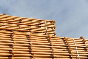 Piles of neatly arranged wooden planks showcase the quality of timber prepared for construction activities in bright daylight photo