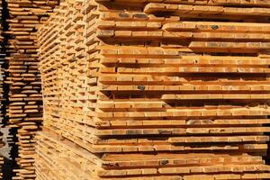 Sturdy wooden planks are neatly stacked in a lumber yard, showing various textures and hues under bright daylight conditions photo