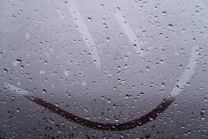 A joyful smiley face artfully etched on a fogged glass window is surrounded by raindrops, bringing warmth to a dreary day photo