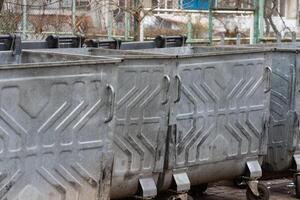 Rows of metal garbage containers filled with trash bags stand in an urban setting, highlighting the need for effective waste management solutions photo