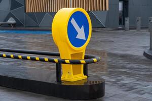 In an urban plaza, a vibrant yellow sign directs foot traffic with its clear arrow design amidst modern structures and wet pavement photo