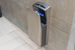 This automatic hand dryer is positioned in a sleek bathroom, showcasing modern sanitation technology for efficient drying photo