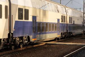 A sleek, double-decker electric train pulls into a busy railway station platform as sunlight bathes the scene in warm tones photo