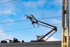 Powerful overhead gears of a modern train poised to connect with high voltage lines against a bright blue sky photo