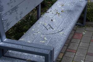 A weathered bench lies blanketed in snow, revealing subtle patterns and surrounded by frozen stones and sparse greenery in winter's chill photo