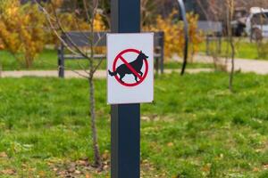 A clear warning sign is visible in a park, indicating that dogs are prohibited in this area to prevent excrement and ensure visitor safety photo