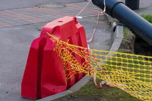 A red construction safety barrier is placed along the sidewalk, marked with caution tape and netting to alert pedestrians in the urban area photo