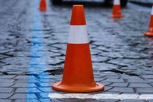Traffic cones are set up in a temporary construction area, creating a safety zone amid wet cobblestones and rainy urban conditions photo