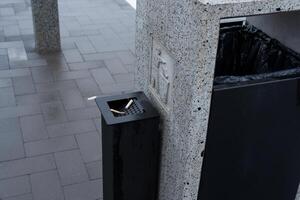 A public space features a solid waste container with a designated area for cigarette disposal, promoting environmental conservation efforts photo