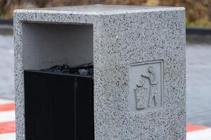 A concrete garbage container stands near water, promoting proper disposal of waste, including recycling and cigarette butts for clean surroundings photo