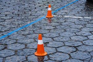 Traffic cones are positioned on a wet cobblestone street marking a construction zone in an urban area during rain photo