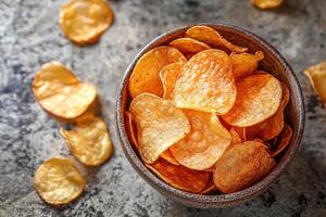 Flat lay photo of savory potato chips in ceramic bowl, surrounded by broken chip pieces for appetizing and rustic presentation