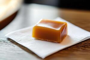 Close-up single caramel candy on crisp white napkin, captured with soft lighting to highlight glossy texture and rich color of caramel. dessert menus, product packaging and confectionery branding photo
