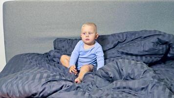 A joyful baby sits happily on a cozy bed adorned with fluffy, soft bedding, embodying pure curiosity and innocence that truly adds warmth to the atmosphere of this lovely room video