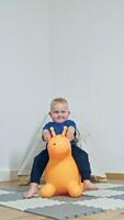 A cheerful toddler, excited and playful, enjoys riding a colorful orange inflatable snail toy, showcasing the joy of childhood in a safe and cozy indoor atmosphere video
