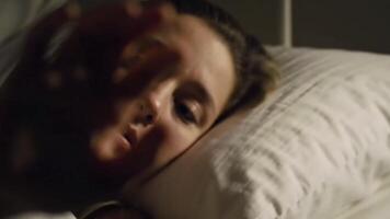 The subject lies awake with their hand outstretched into the darkness beside them. video