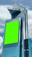 Green chroma key blank vertical billboard mock up in city center for advertising on skyscrapers office with beautiful clouds background video