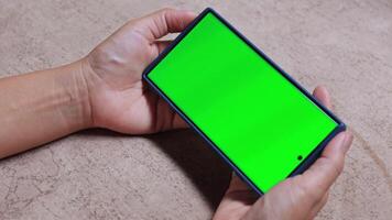 Hands holding a smartphone with green screen in horizontal position, ideal for adding custom content or mockups, Shot on a neutral surface for tech and advertising use, close-up video