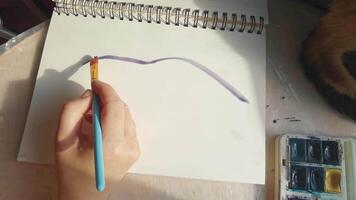 Female hand creating abstract watercolor art with brush and palette on spiral notebook page. video