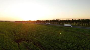 Traffic On The Highway At Sunset Aerial View. Trucks driving on the highway, side view. Scenic drive along the green fields at sunset video