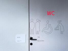 Modern public restroom door with illuminated WC sign, inclusive pictograms for men, women, disabled persons, and baby care. Accessible and universal design in public infrastructure photo