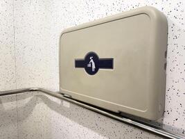Wall mounted baby changing table in a public restroom with a stainless steel safety bar. Modern accessible facility for parents with infants, promoting convenience and inclusive design photo