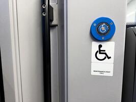 Modern accessibility assistance button with blue wheelchair symbol and maintenance staff call sign mounted on light gray wall inside public transportation, symbolizing inclusive design photo