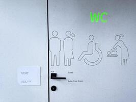 Modern accessible WC door with glowing green signage and clear pictograms for men, women, disabled users, and baby care. Inclusive design promoting visibility and universal access photo