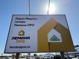Kursk, Russia, April 21, 2025 Billboard in Russian shows the rebranding of Leroy Merlin to Lemana PRO in Russia, with both logos visible and clear blue sky above a crowded parking lot photo