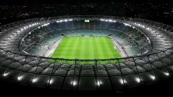 Aerial view of a bright illuminated stadium at night with green grass and empty seats visible video