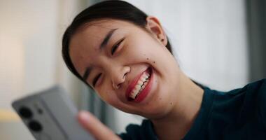 Happy Asian woman sitting on a sofa enjoying playing with mobile phone with a smiling and laughing face. video