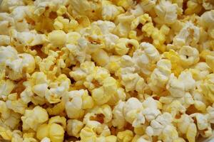 Close-up of freshly popped buttered popcorn. A golden, crispy, and tasty snack ideal for movie nights or food-related content. High-resolution macro image with vibrant yellow and white tones. photo