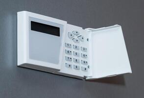Security system keyboard with buttons and plastic cover mounted on a gray textured wall. photo