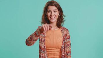 I choose you. Young Caucasian woman pointing finger to camera, looking with playful happy expression, making winner choice, showing direction. Brunette girl isolated on blue studio background indoors video