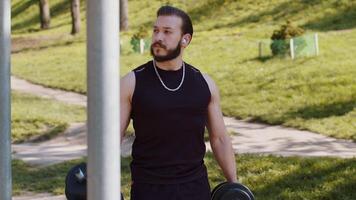 Athletic lebanese man in sportswear doing arms weight lifting dumbbells exercises, pumping up arm bicep muscles. Young guy on playground. Sports, health, fitness routine, workout. Strength motivation video