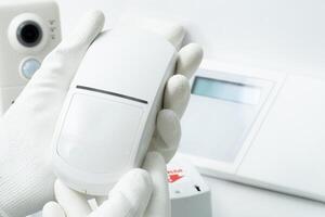 The left hand of a man in a white glove holds a motion sensor of security systems photo