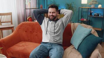 Tired man lying down on comfortable couch, taking a rest, daytime nap. Portrait of carefree Caucasian guy holding hands behind head relaxing, falling asleep at home apartment living room on sofa video