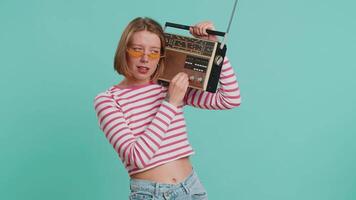 Woman in sunglasses using retro tape record player to listen music, disco dancing of favorite track, having fun, entertaining, fan of vintage technologies. Girl in crop top isolated on blue background video