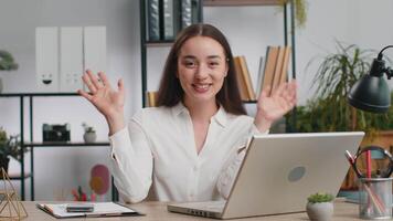 Hello. Caucasian business woman working on laptop computer smiling friendly at camera, waving hands gesturing hi greeting or goodbye, welcoming with hospitable expression at home office workplace desk video