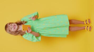 Young preteen child girl kid use mobile smartphone typing browsing say Wow yes found out great big win good news celebrate doing winner gesture. Little children on studio yellow background. Vertical video