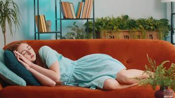 Tired young redhead woman lying down in bed taking a rest at home. Portrait of carefree girl napping, falling asleep on comfortable orange sofa with pillows. Closed her eyes enjoy daytime nap alone video