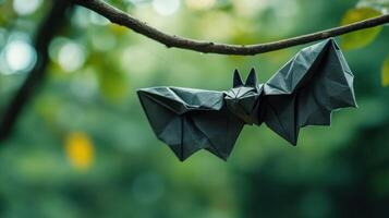An origami bat is hanging from a small brown branch photo