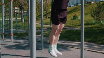 Athletic man in sportswear doing pull-ups exercises on horizontal bar with help of elastic expander. Young guy pumping up back muscles on playground. Sport health fitness routine workout. Bodybuilding video