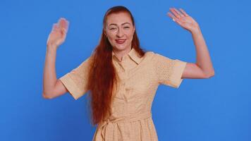 Come here, join us. Welcome. Redhead attractive woman showing inviting gesture with hands, ask to join, beckoning to coming, gesturing hello, goodbye. Adult girl isolated on blue studio background video