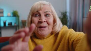 POV of senior grandmother woman making online selfie call talking waving hand looking at camera at home apartment indoors. Communication, meeting. Elderly blogger making smartphone conversation video